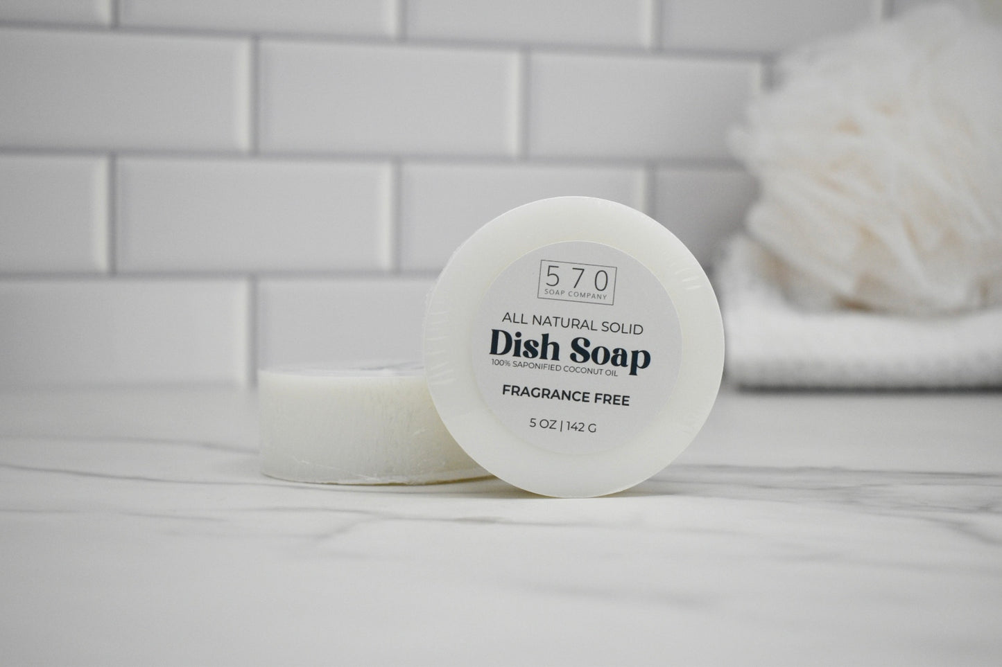 All-natural solid dish soap container on a bathroom counter with a tiled wall background.
