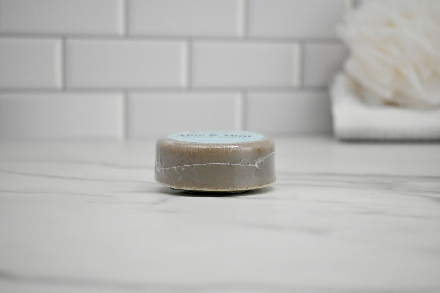 Small container of soap on a bathroom counter with tiled wall in the background