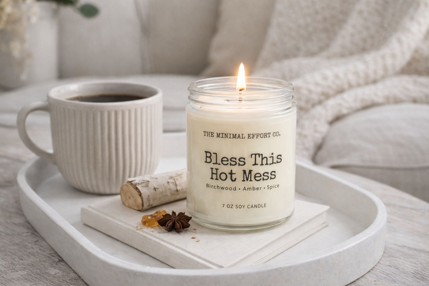 Candle labeled 'Bless This Hot Mess' on a tray with a mug of tea and decorative items.