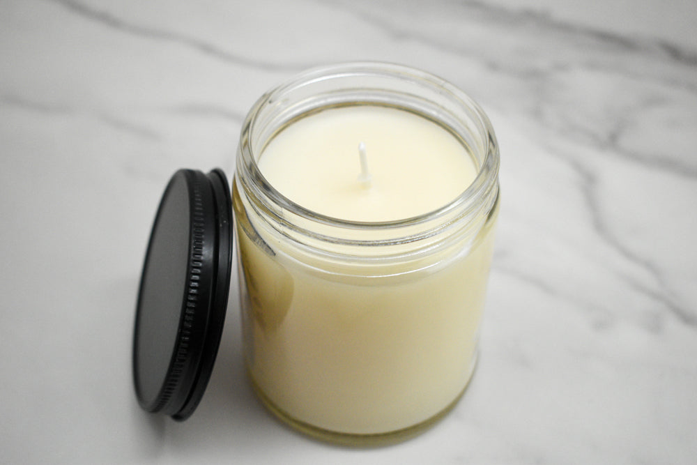 Candle in a glass jar with a black lid on a gray surface