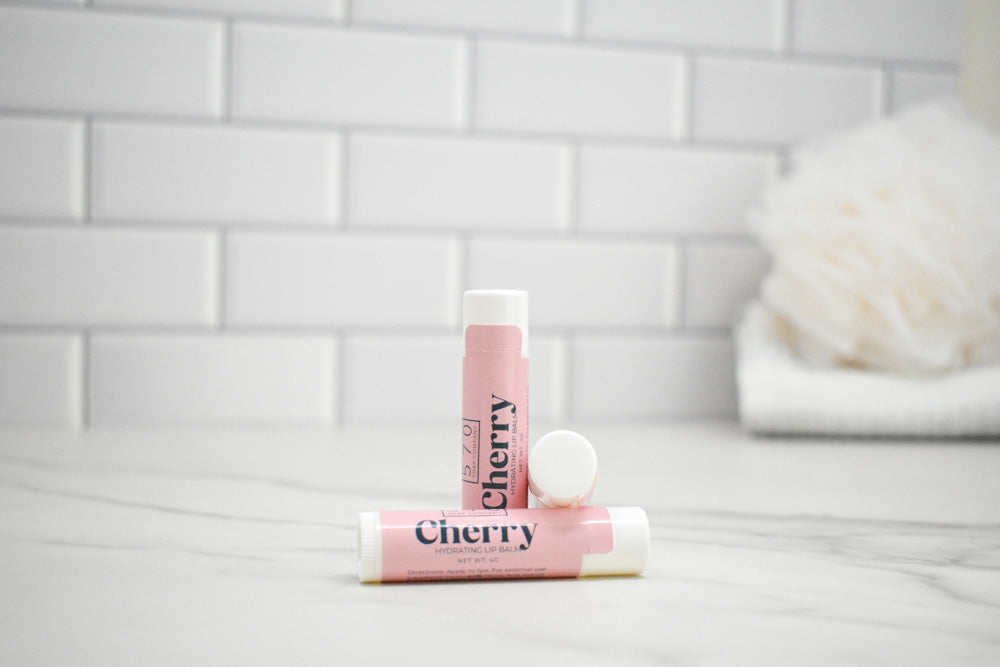 Two pink lip balms labeled 'Cherry' on a white surface with a tiled wall background.
