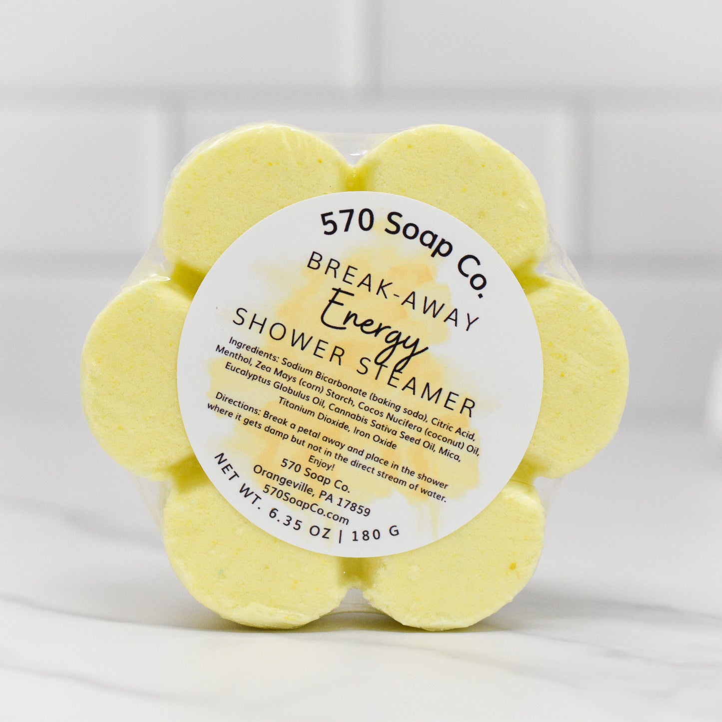 A 6.35 oz (180g) package of flower-shaped Energy Shower Steamers - Citrus from 570 Soap Co., infused with revitalizing citrus essential oils, featuring ingredients and contact details on a white tiled background.
