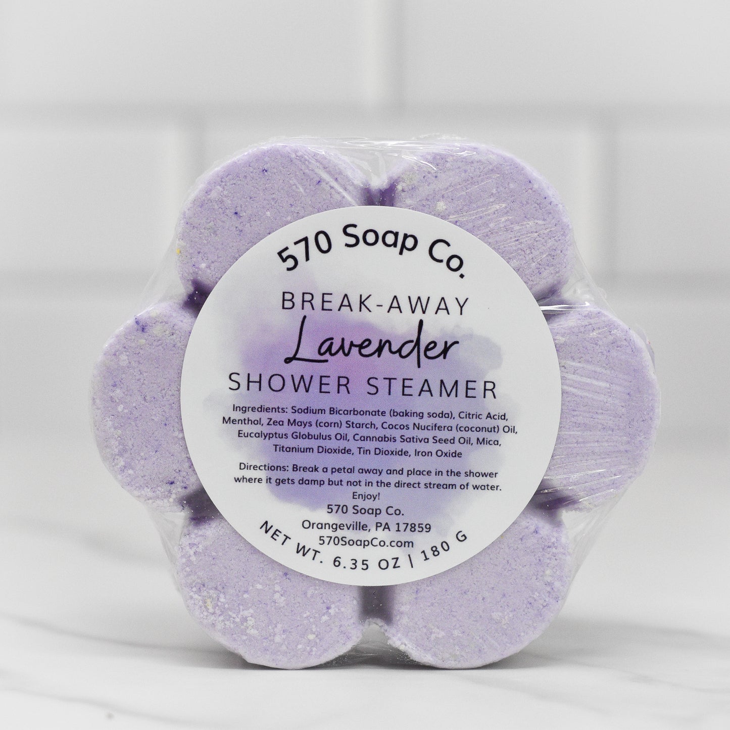 The Relax Shower Steamer - Lavender from 570 Soap Co. provides a soothing shower experience. The flower-shaped steamer's label includes the ingredients, usage instructions, contact information, and its weight of 6.35 oz (180 g), all crafted to elevate your menthol invigoration journey.