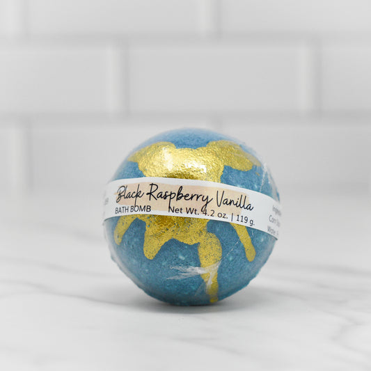 A relaxing teal bath bomb from 570 Soap Co., named Black Raspberry Vanilla, weighs 4.2 ounces (119 grams) and rests on a white marble surface with a white tiled wall behind it.