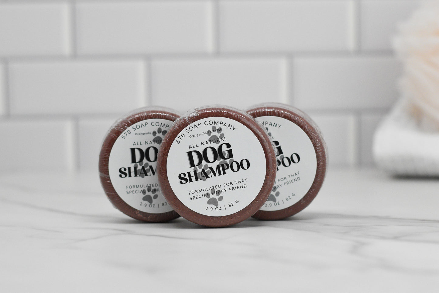Three bars of the Dog Shampoo Bar - All Natural, featuring a calming lavender aroma, are showcased on a marble surface. The labels prominently display the name 570 Soap Co. A white tiled wall in the background accentuates the gentle cleansing formula ideal for your furry friend.