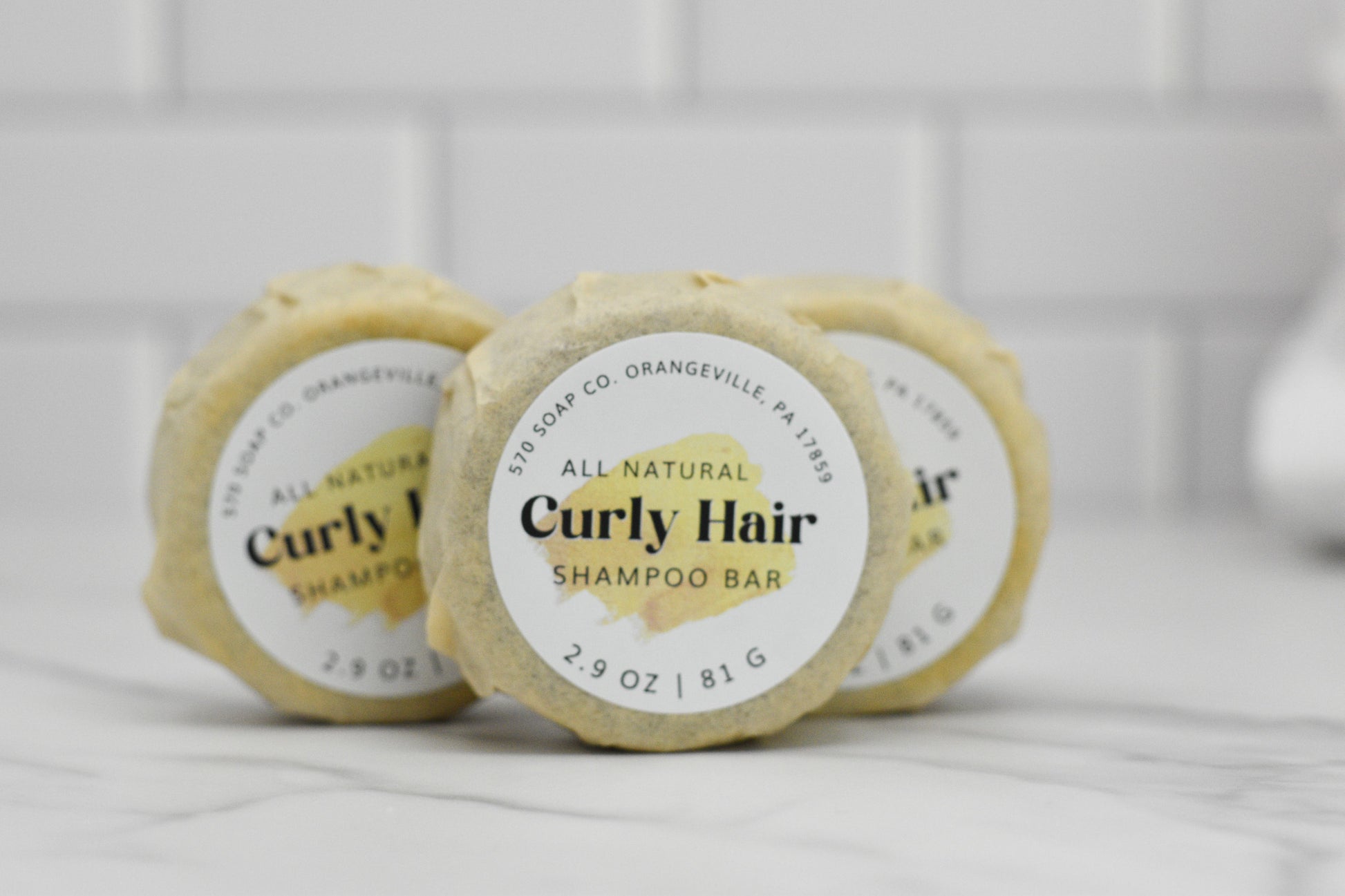 Three round packages of the Curly Hair Shampoo Bar - All Natural from 570 Soap Co. are neatly arranged on a white marble surface against a white tiled background. Ideal for curly hair, each bar is labeled with 2.9 oz / 81 g.