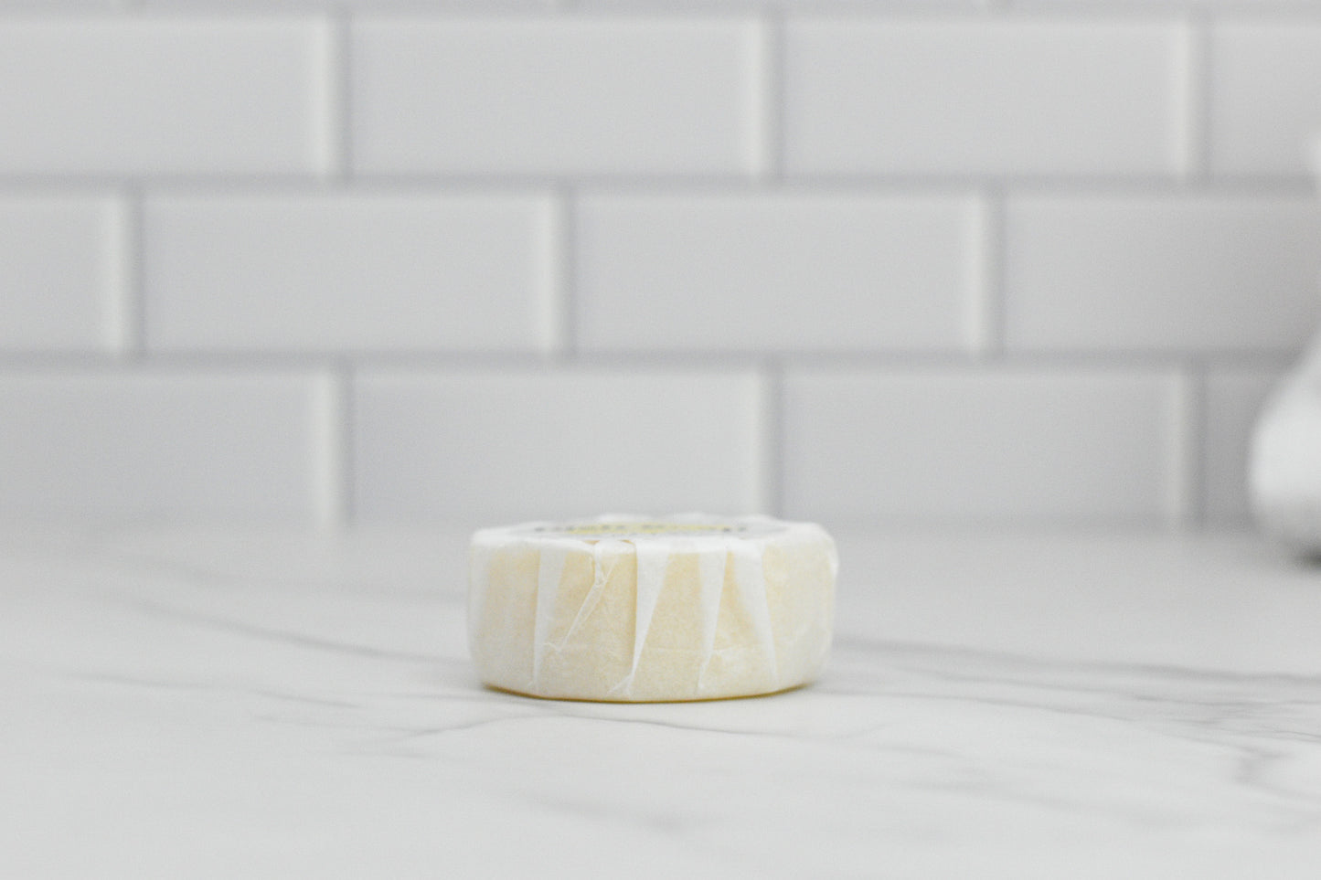 The Zesty Lemon Dish Soap Bar from 570 Soap Co., made with all-natural ingredients, rests on a marble countertop against a white subway tile backsplash, making it the perfect eco-friendly kitchen essential.