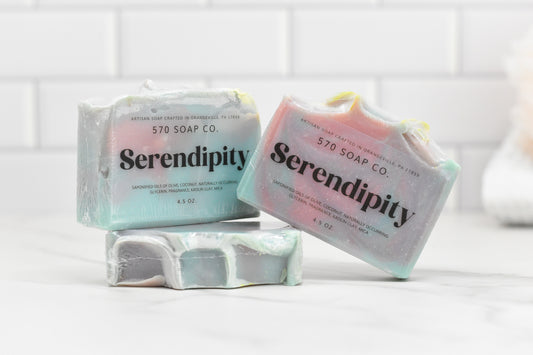 Three vibrant bars of Serendipity Bar Soap by 570 Soap Co. are showcased, formulated with a luxurious moisturizing blend. The pastel tones stand out against a white tile backdrop, highlighting a clean and fresh aesthetic.