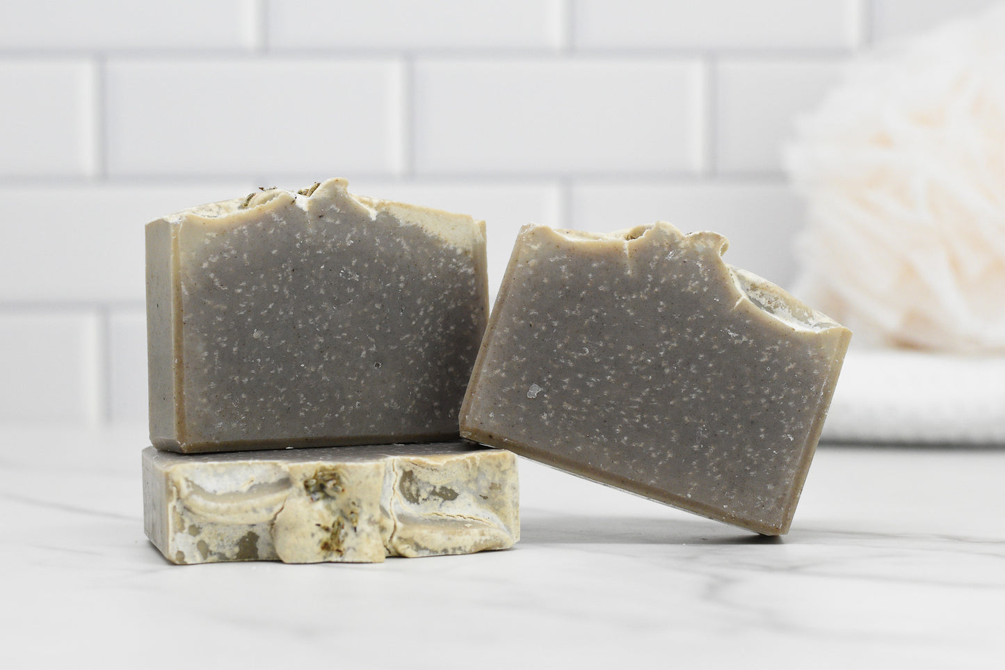 Two bars of the Lavender Essential Oil Bar Soap - All Natural by 570 Soap Co. are stacked on a white marble countertop. The textured surface, complemented by the backdrop of a white tiled wall, exudes a clean, minimalist aesthetic.