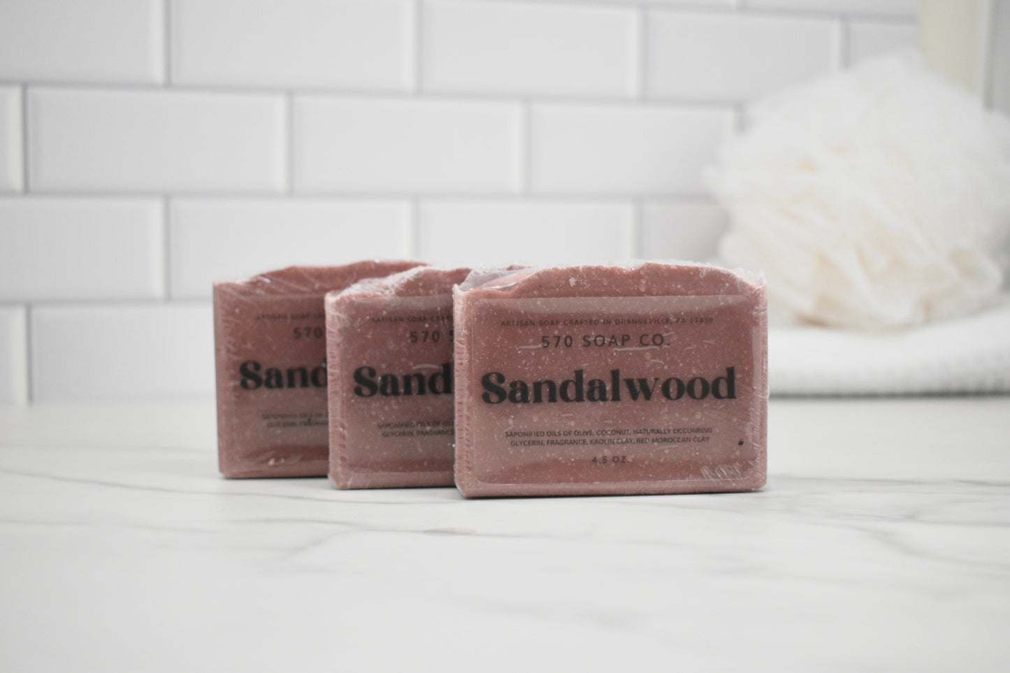 Three bars of Sandalwood soap from 570 Soap Co on a white surface with a tiled wall background.
