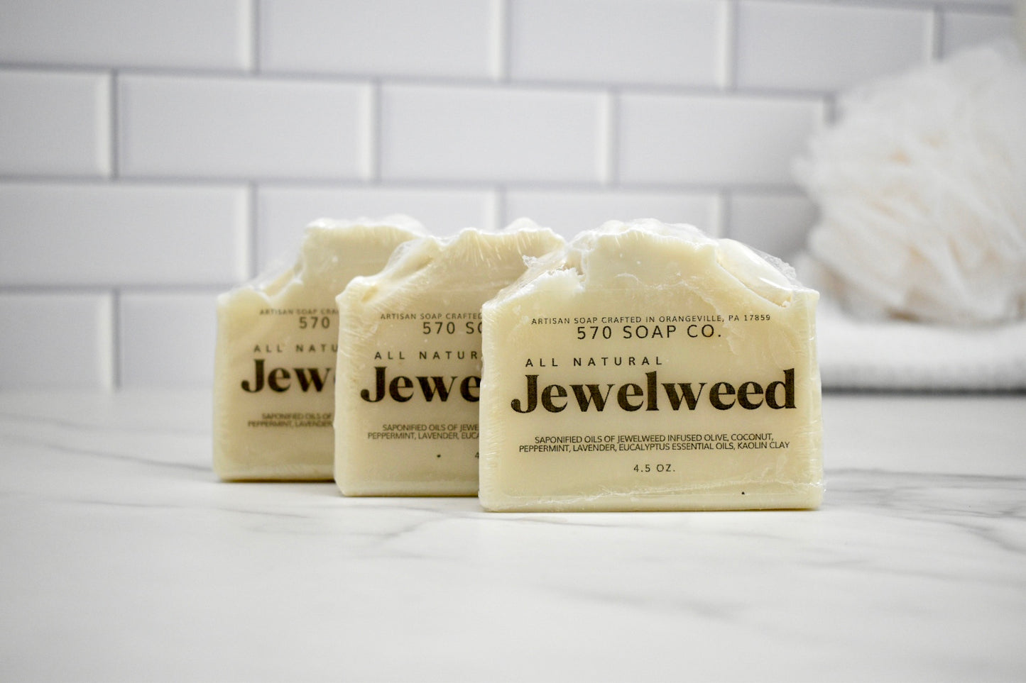 Three bars of Jewelweed soap from 570 Soap Co on a white surface with a tiled wall background.