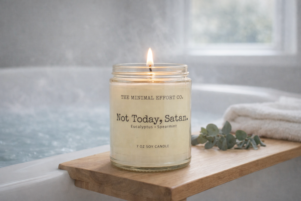 Candle labeled 'Not Today, Satan' on a wooden shelf by a bathtub.
