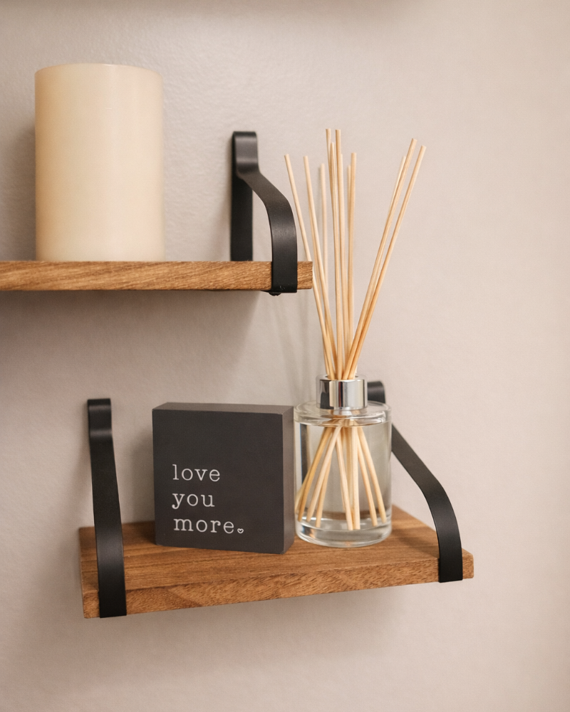 Wooden shelves with a candle, diffuser, and small sign against a beige wall.