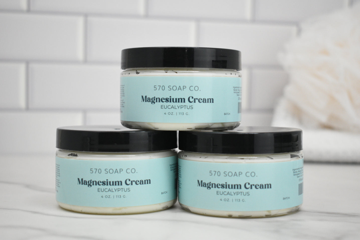 Three jars of 570 Soap Co. eucalyptus magnesium cream on a white surface with a tiled wall background.