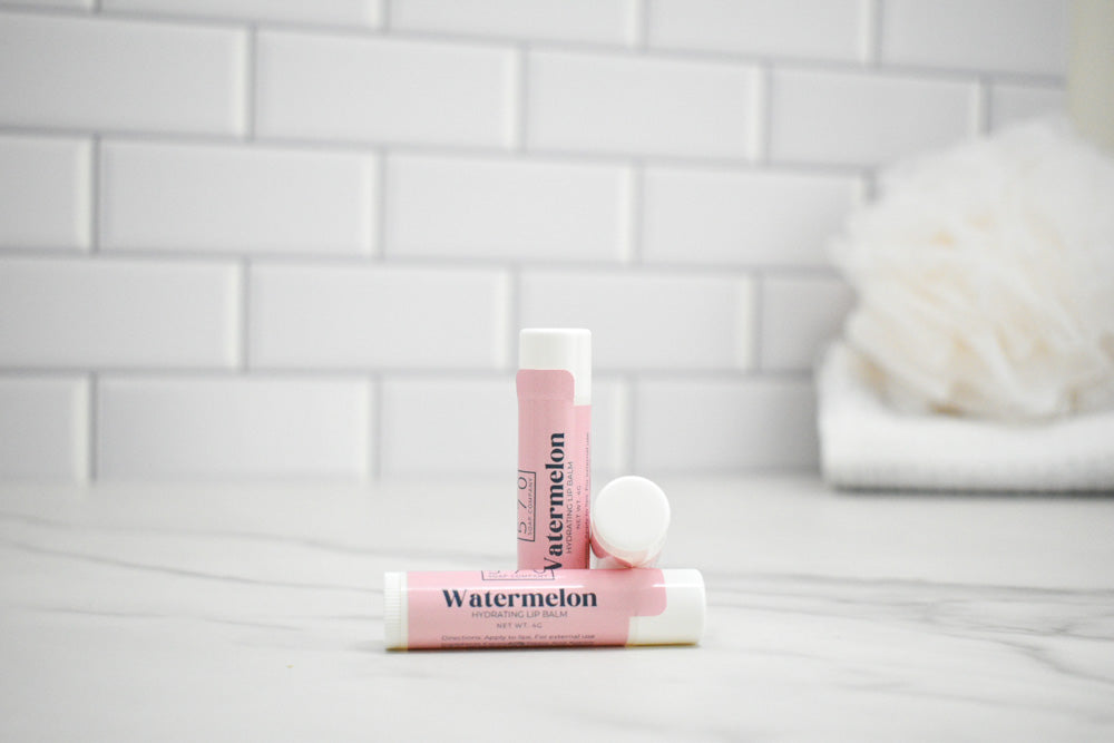 Two lip balms labeled 'Watermelon' on a bathroom counter with a tiled wall background.