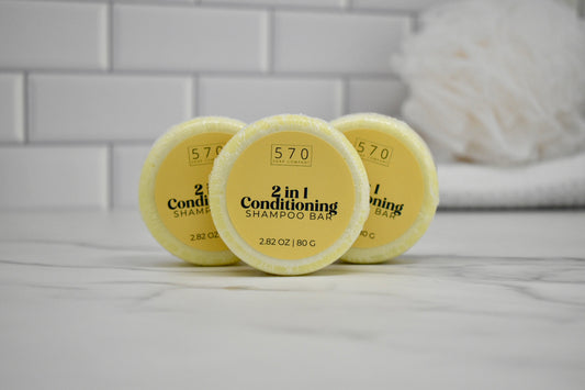 Three yellow 2-in-1 conditioning shampoo bars on a white surface with a tiled wall background.