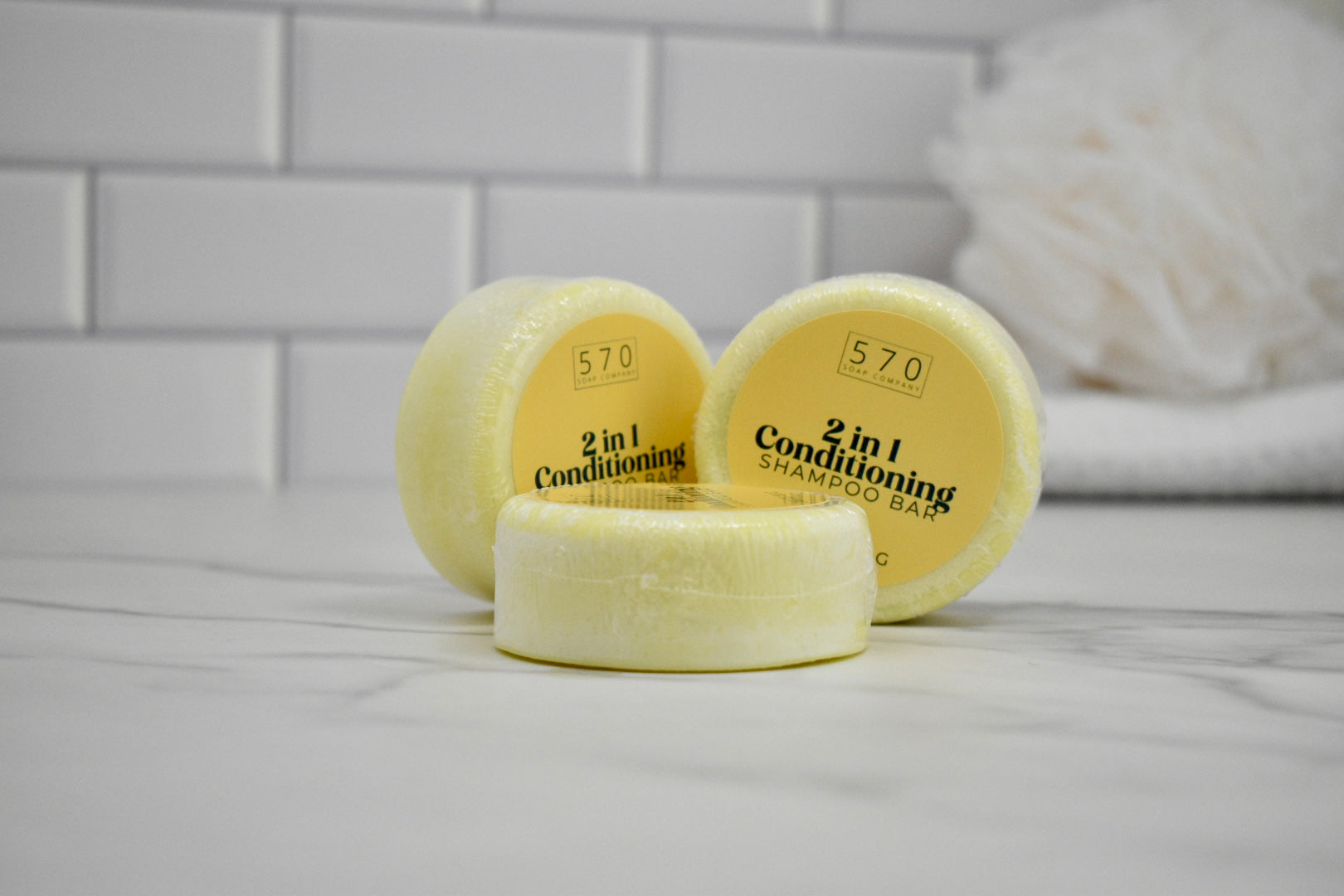 Three yellow 2-in-1 conditioning shampoo bars on a white surface with a tiled wall background.