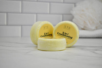 Three yellow 2-in-1 conditioning shampoo bars on a white surface with a tiled wall background.