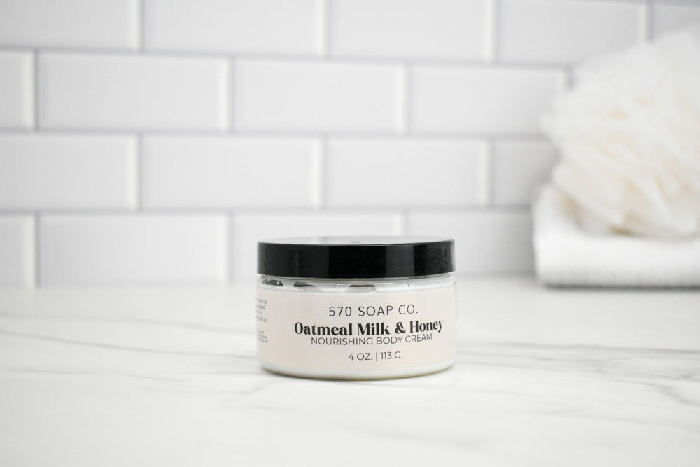 Jar of 570 Soap Co. Oatmeal Milk and Honey body cream on a white surface with a tiled wall background.
