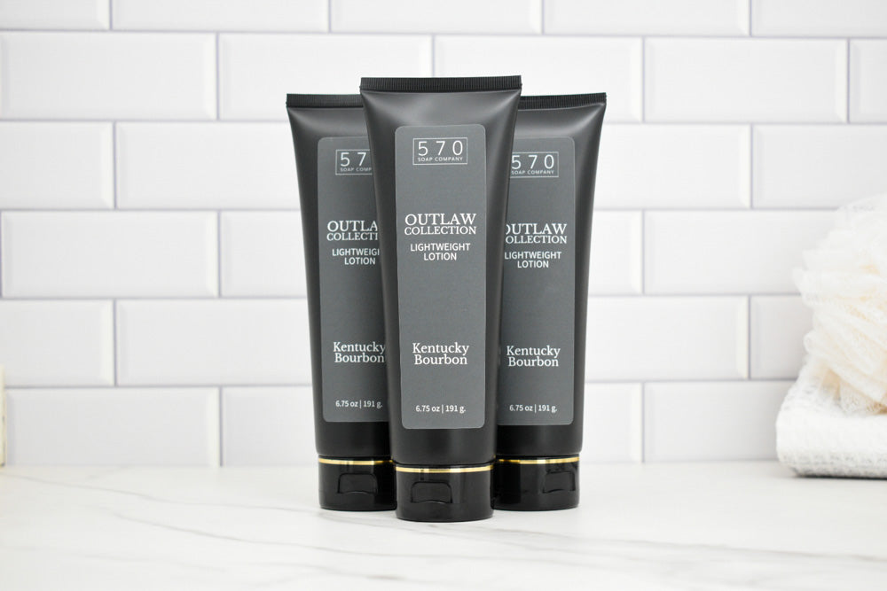 Three black tubes of Outlaw Collection Kentucky Bourbon Lightening Lotion on a white tiled background.