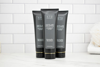 Three black tubes of Outlaw Collection Kentucky Bourbon Lightening Lotion on a white tiled background.