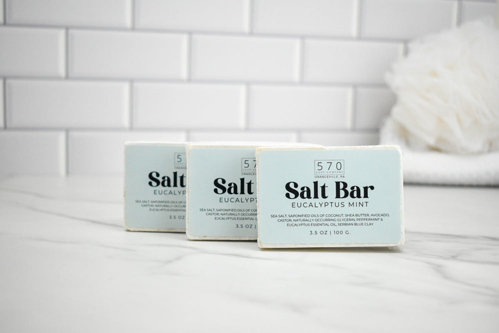 Three bars of Salt Bar Eucalyptus Mint soap on a white surface with a tiled wall background.