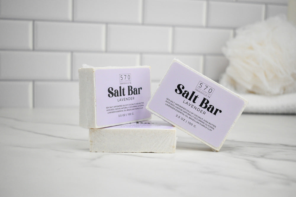 Two salt bars with lavender scent on a white surface against a tiled wall background.