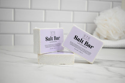 Two salt bars with lavender scent on a white surface against a tiled wall background.