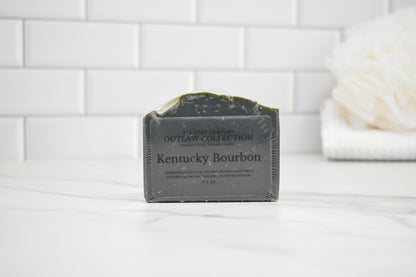 Bar of soap labeled 'Kentucky Bourbon' from the Outlaw Collection on a white surface with a tiled wall background.