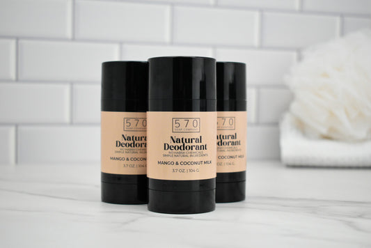 Three 570 Natural Deodorant sticks on a white surface with a tiled wall background.