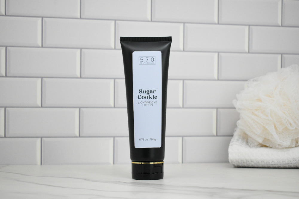 Black tube of 570 Sugar Cookie body lotion on a white surface with a tiled wall background