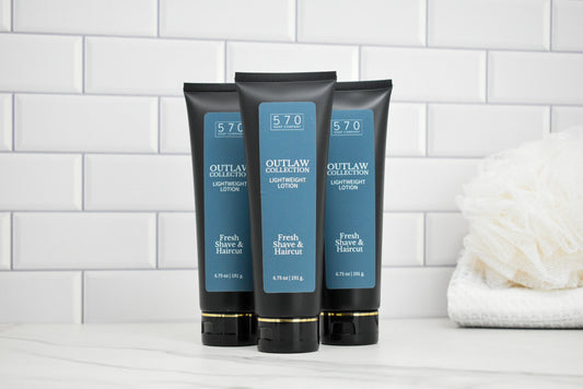 Three bottles of 570 Outlaw Collection lotion on a white tiled wall background.