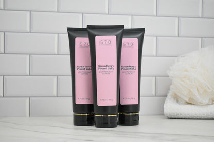 Three black tubes of Strawberry Pound Cake lotion on a white surface with a tiled wall background