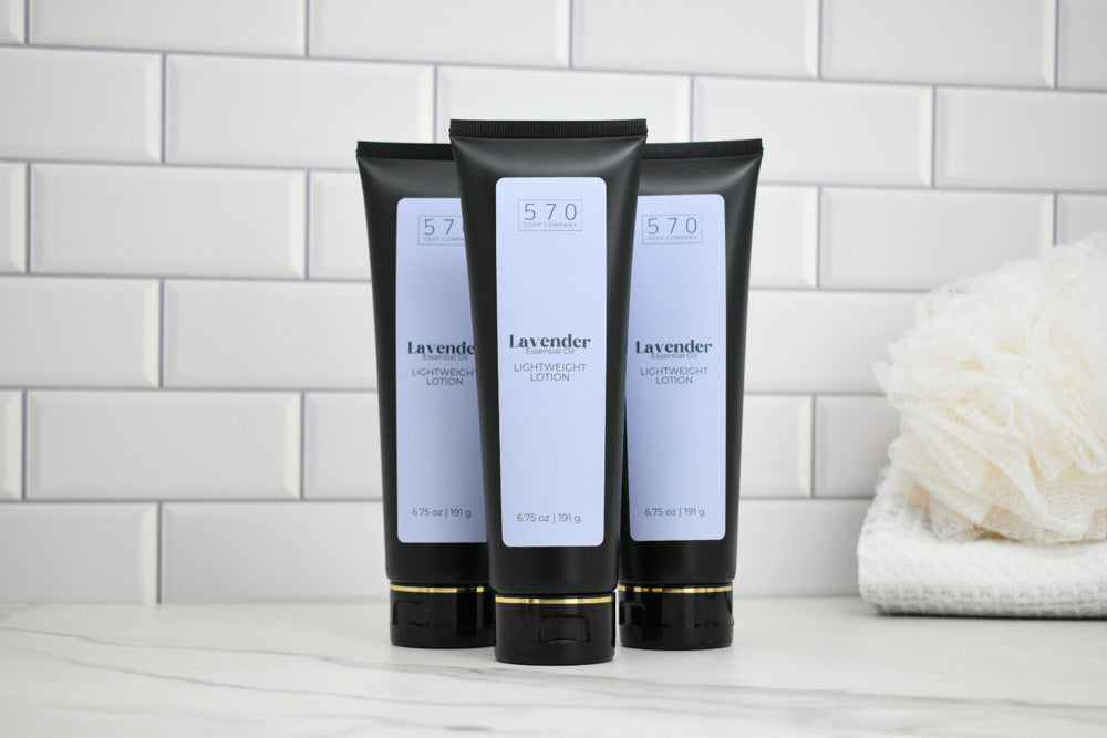 Three black tubes of Lavender body lotion on a white surface with a tiled wall background.