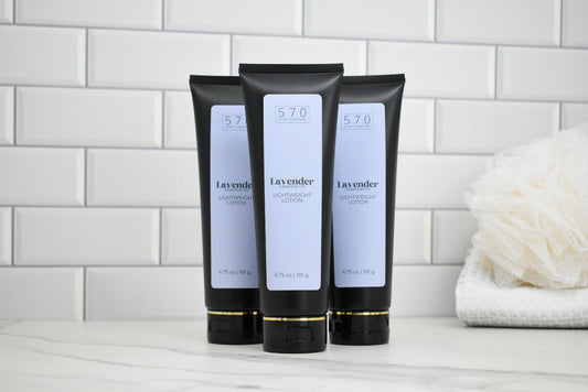 Three black tubes of Lavender body lotion on a white surface with a tiled wall background.