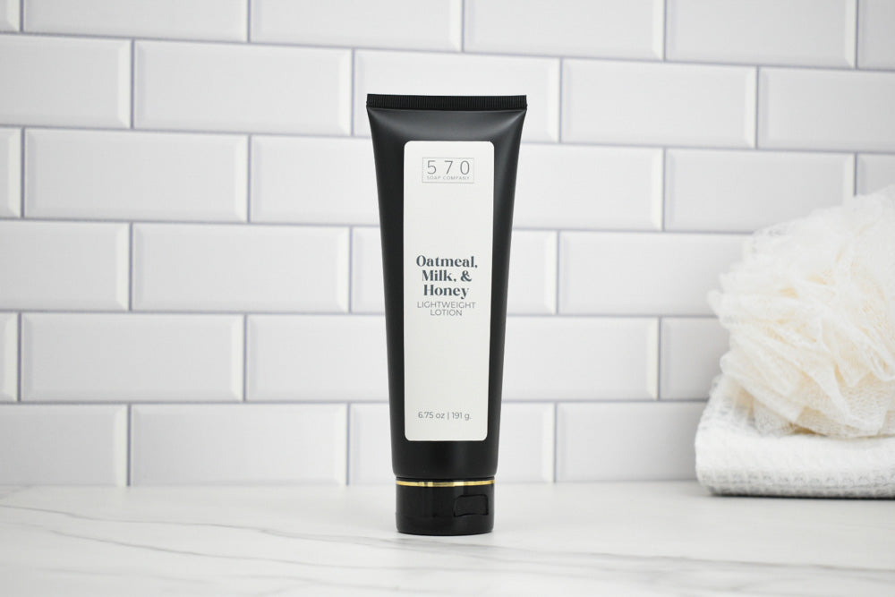 Black tube of 'Oatmeal, Milk, & Honey' lotion on a white tiled bathroom shelf.