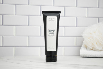 Black tube of 'Oatmeal, Milk, & Honey' lotion on a white tiled bathroom shelf.