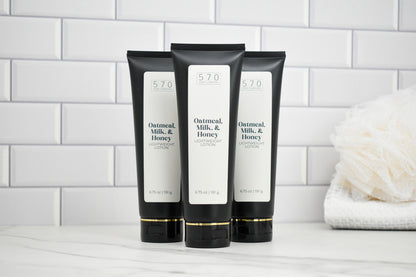 Three black tubes go Oatmeal Milk and Honey lotion on a white surface with a tiled wall background