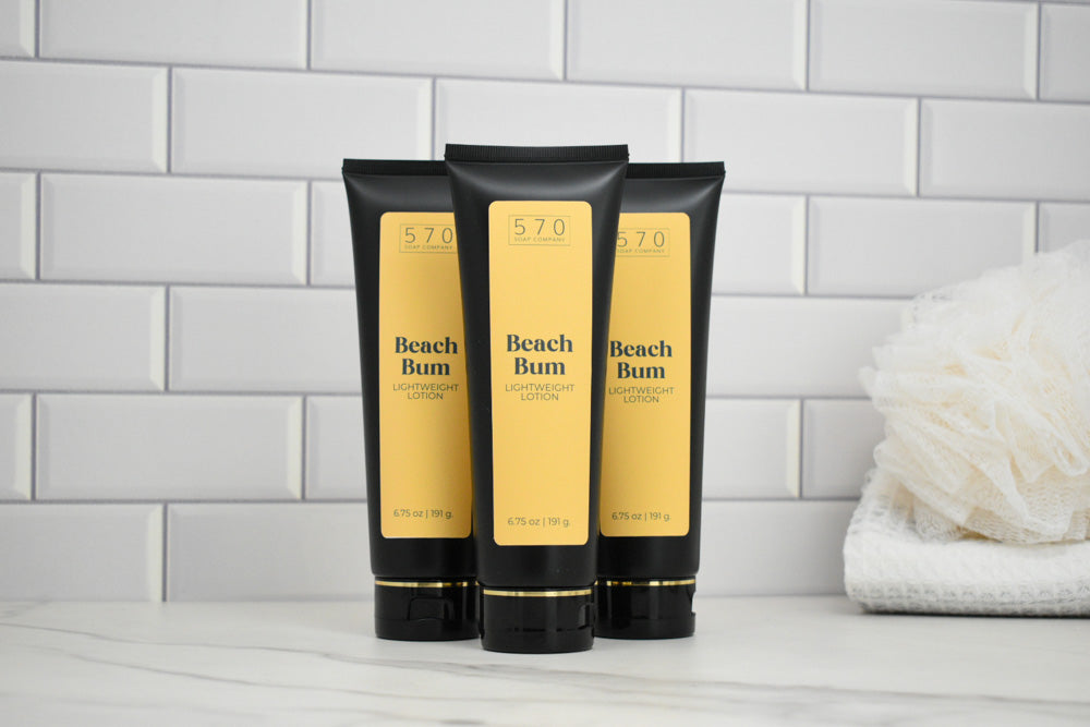 Three Beach Bum Lotion bottles on a bathroom counter with a tiled wall background.