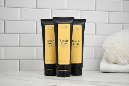 Three Beach Bum Lotion bottles on a bathroom counter with a tiled wall background.