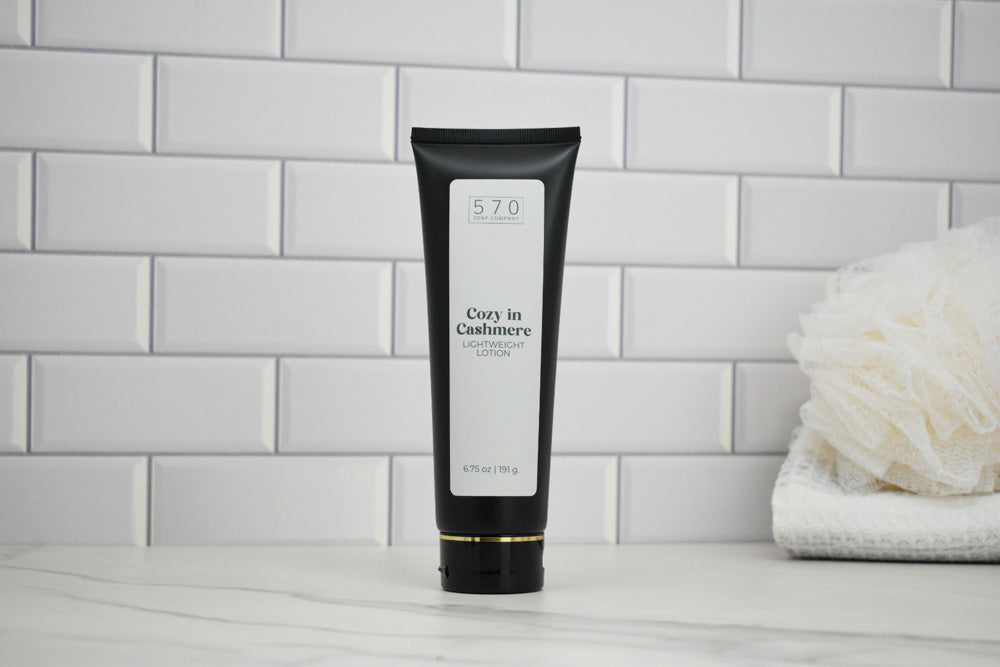 Black tube of Cozy in Cashmere lotion on a bathroom counter with white tiles in the background