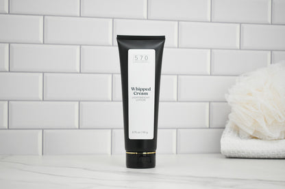 Black tube of whipped cream lotion on a white tiled wall background