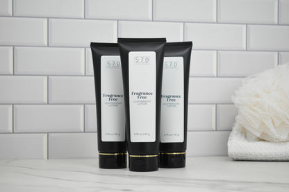 Three black tubes of Fragrance Free lotion on a bathroom counter with a white tiled wall background.