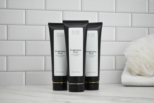 Three black tubes of Fragrance Free lotion on a bathroom counter with a white tiled wall background.
