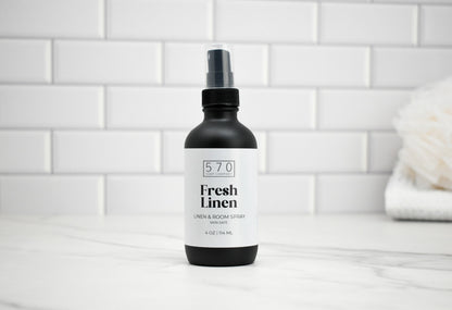 Bottle of 570 Fresh Linen spray on a white tiled bathroom counter.