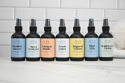 Row of 8 black spray bottles with labels on a white surface.