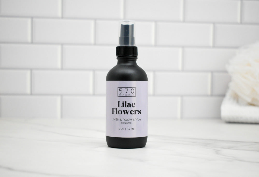 Bottle of 'Lilac Flowers' room spray with a white label on a tiled bathroom floor.