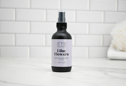 Bottle of 'Lilac Flowers' room spray with a white label on a tiled bathroom floor.