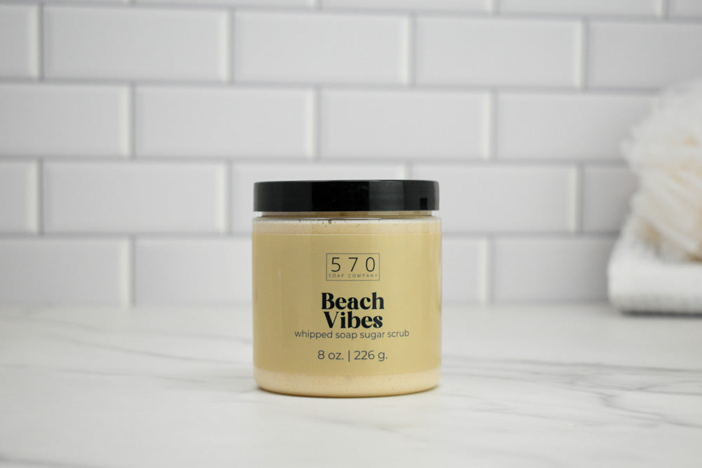 Jar of 'Beach Vibes' whipped sugar scrub with '570' branding on a tiled bathroom shelf.