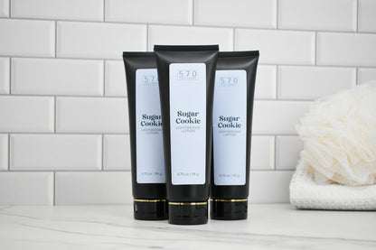 Three black tubes labeled '570 Sugar Cookie' on a white surface with a tiled wall background.